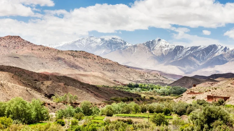 Fertile green fields, earthen Berber villages, and snow-capped Atlas peaks in the background.
